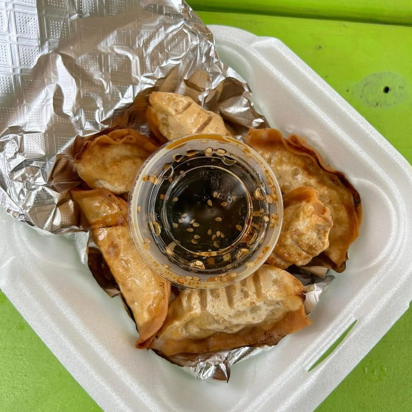 Fried Filipino dumplings with a side of dipping sauce in a white takeout container.