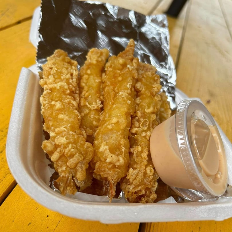Crispy golden-brown fried shrimp with a side of dipping sauce in a white takeout container.