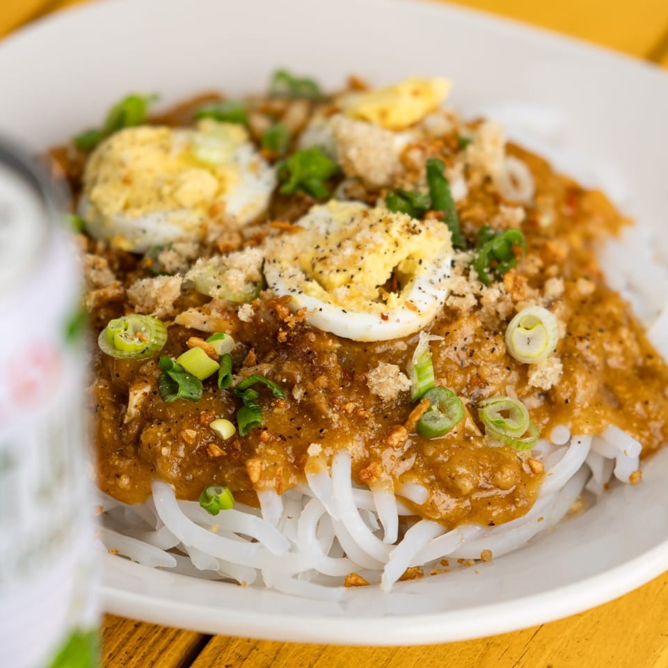 Filipino Palabok noodles with a rich orange sauce, sliced eggs, green onions, and crispy toppings.