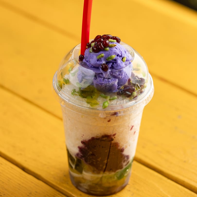 Filipino Halo-Halo dessert with purple ube ice cream, red beans, and a red straw.