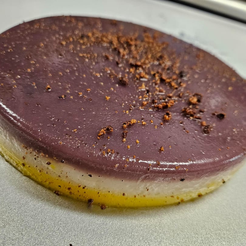 A Filipino dessert with layers of purple, white, and yellow, topped with brown crumbs.