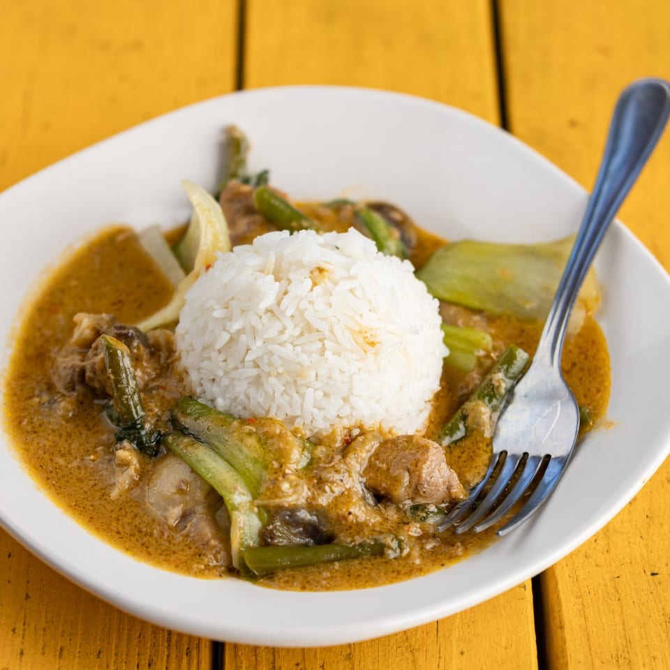 Filipino Kare-Kare with rice, meat, and vegetables in peanut sauce, served on a white plate.